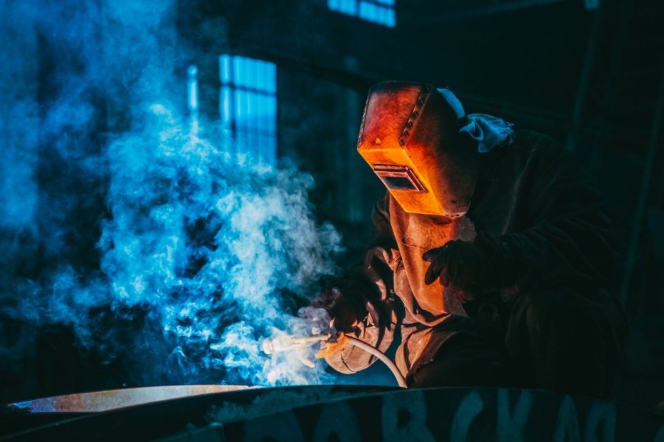 Soudeur au masque et aux gants soudant dans un nuage de fumée bleue