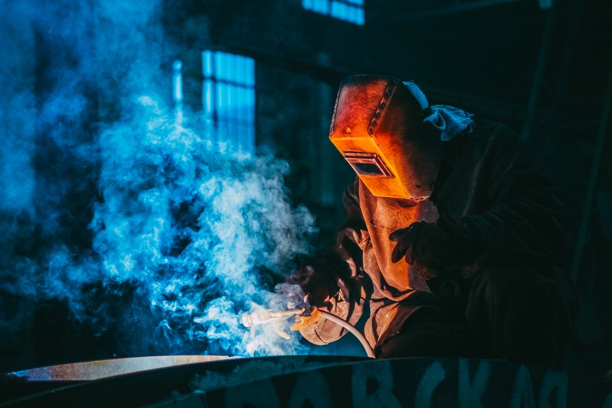 Soudeur au masque et aux gants soudant dans un nuage de fumée bleue