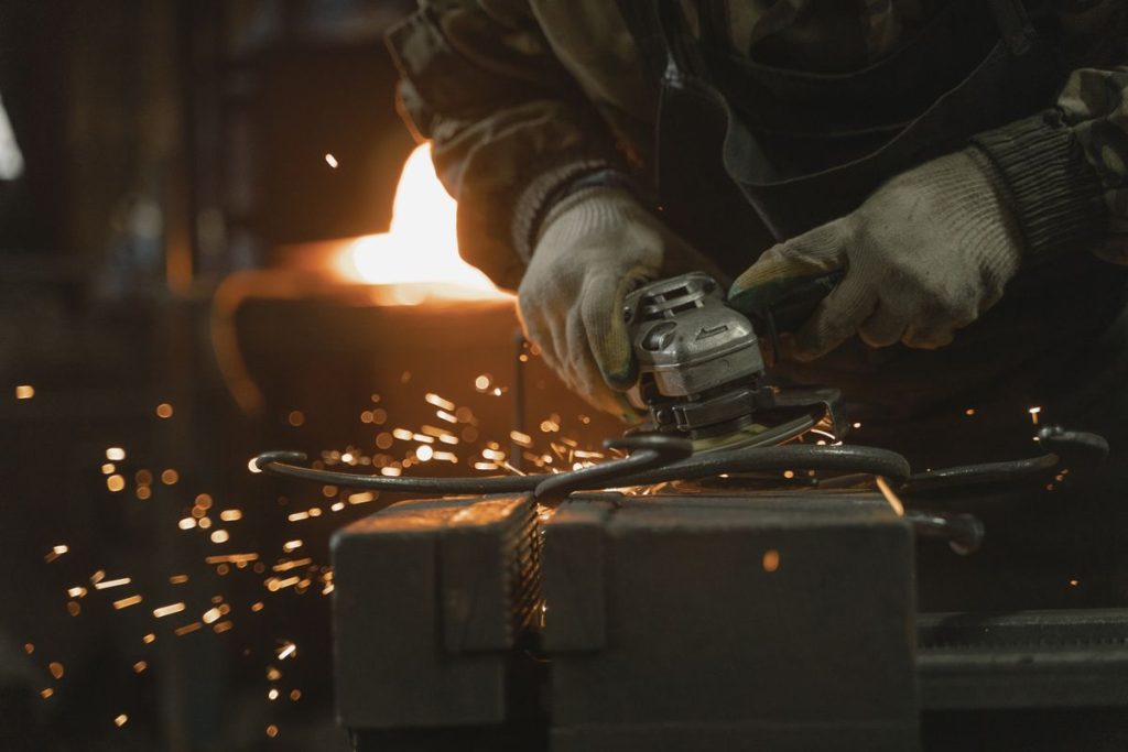Mains gantées meulant du métal dans une gerbe d'étincelles à l'atelier