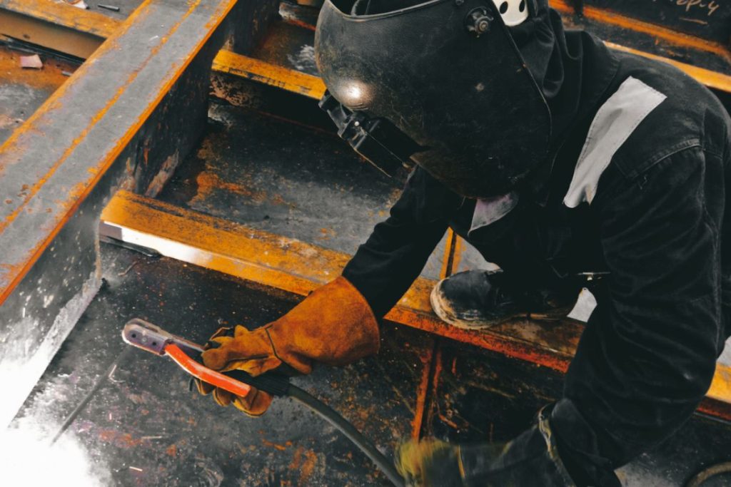 Soudeur ganté brossant un cordon de soudure sur une structure en acier