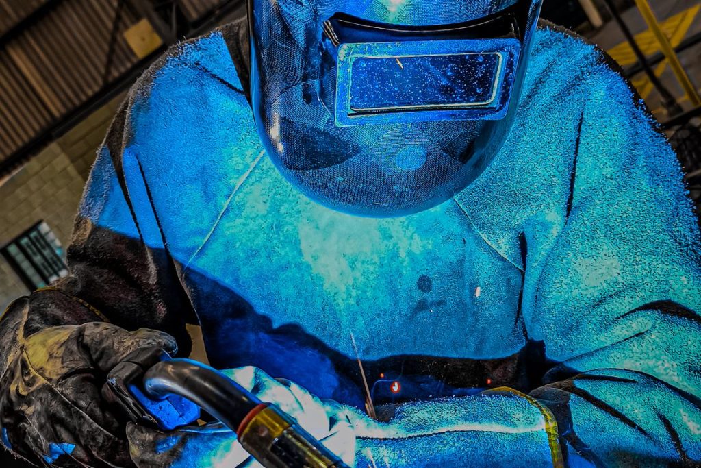 Gros plan d'un soudeur tenant le pistolet MIG, lumière d'arc bleue
